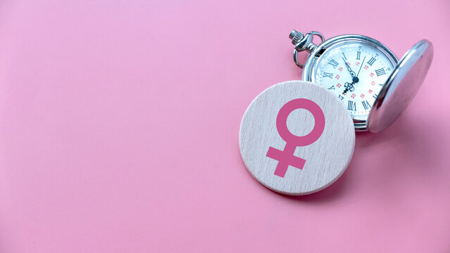 Menopause concept. Women symbol over a watch. Healthcare and medical for women. Pink background with copy space.