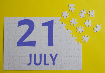 21 july calendar date on a white puzzle with separate details. Puzzle on a yellow background with a blue inscription
