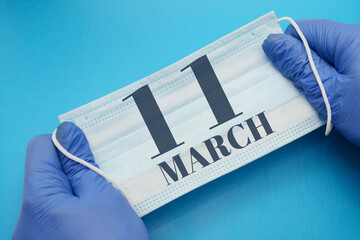 11 march day of month. Doctor holding an antivirus mask in blue medical gloves on blue background. Protection from disease