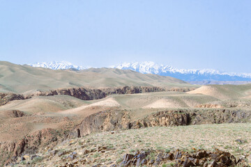 High mountains with snow and blue sky are visible in the background, near the border with China, Black Canyon, Kazakhstan. High hills and a lot of grass along with stones with the river near downhill