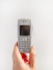 A hand holding old mobile phone on white background, early wireless digital technology, communication device