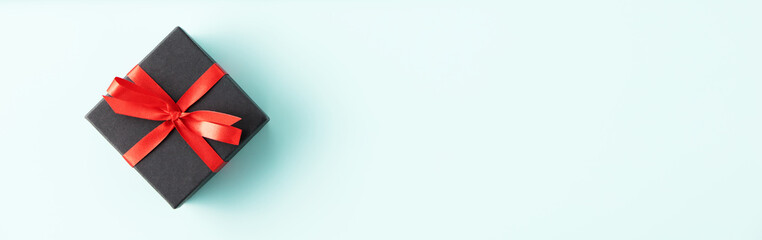 Gift box with red satin ribbon and bow on blue background. Holiday gift with copy space.