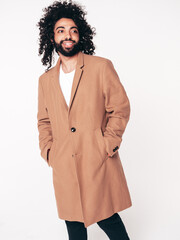 Handsome smiling hipster model.  Unshaven Arabian man dressed in brown coat clothes. Fashion male with long curly hairstyle isolated on white in studio. Cheerful and happy