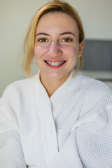 Positive girl with natural beauty face with out make up, wearing braces and a white robe, smiles at the camera after beauty procedures, skin rejuvenation, in a beauty clinic, spa salon.