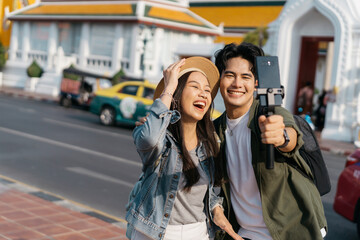Portrait of Asian man and woman couple travelers in relationship taking a selfie video call in front of buddhist temple on street in Bangkok, Thailand, Southeast Asia - carefree and happiness concept - 605136093