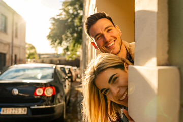 a man and a woman peek out from behind a wall and look at the camera