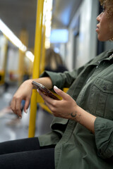 Vertical image of young afro woman traveling by underground and browsing a mobile phone