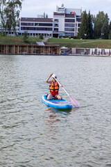 A girl in a life jacket swims on a SUP board. SUP board Stand up paddle girl boarding on lake standing happy on blue water. 