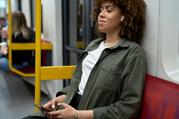 Young afro woman traveling by underground and relaxing with a mobile phone and earphones