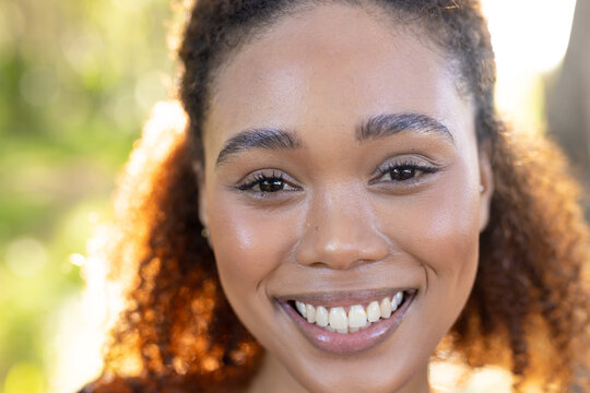 Portrait of happy biracial woman looking at camera and smiling in forest, unaltered