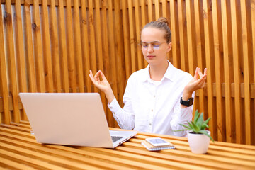Relaxed overworked woman wearing white shirt sitting in outdoor cafe working on laptop trying to...