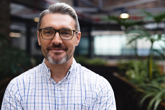 Portrait of happy caucasian businessman looking at camera and smiling at office, unaltered - Powered by Adobe