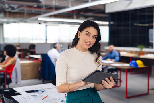 Portrait of happy caucasian businesswoman using tablet and smiling at office, unaltered