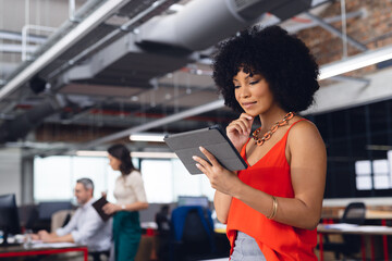 Happy african american businesswoman leaning on desk, using tablet and smiling at office, unaltered