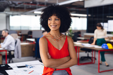Happy african american businesswoman crossing arms, looking away and smiling at office, unaltered