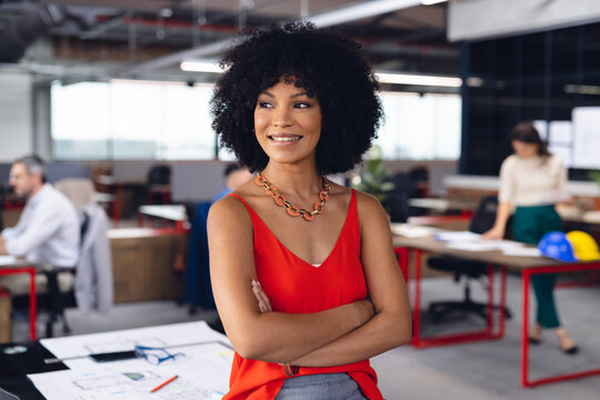 Happy african american businesswoman crossing arms, looking away and smiling at office, unaltered