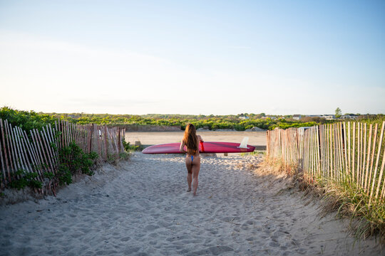 Woman in skimpy bikini walking with her surfboard at sunset