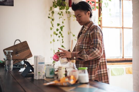 queer asian woman measures baking ingredients in light home kitchen