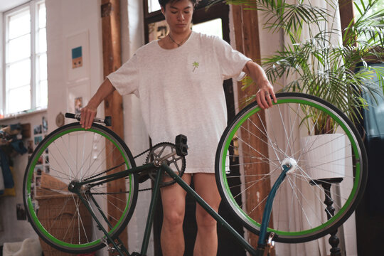 queer woman fixes green vintage bike in wooden studio with plants