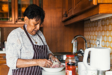 older latin american woman kneading meat cooking in the kitchen