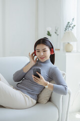 Asian woman dancing to the music playing from laptop on sofa in her home living room, weekend break, relaxation from hard work, drinking coffee. Take a vacation after a hard day's work.