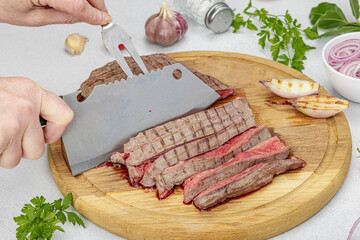 Woman cuts grilled steak. Female hands with knife and two pronged fork. Fresh herbs, vegetables