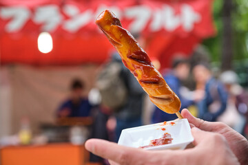 Person holding a Fried Sausage Stick street food at a flea market in Kyoto, Japan.