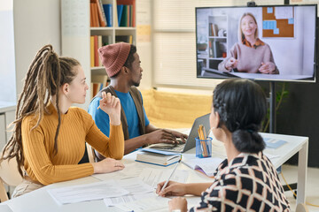 Multiethnic group of students learning English with native speaker during video call on the screen...