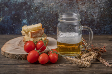 A mug of beer with toasted bread and red cherry tomatoes next to it, with dried ears of corn