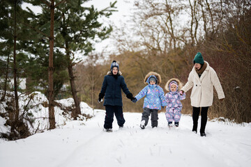 Fototapeta na wymiar Mother with three kids holding hands and walking in winter forest.