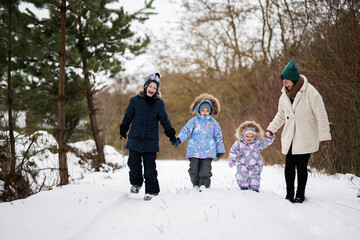 Mother with three kids holding hands and walking in winter forest.