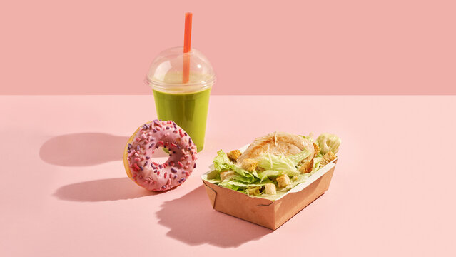 caesar salad in paper box, donut and matcha in plastic cup on pink background