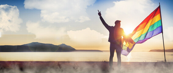 Fototapeta na wymiar LGBT Pride Concept. Silhouette of a man holding a rainbow flag in front of a river in the evening background of the sky and mountains against the morning sun. copy space, banner, website- 3d rendering
