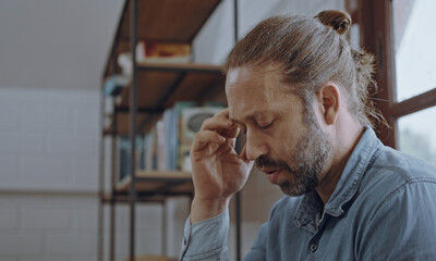 Young worried man using laptop sitting on bed at bedroom.