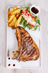 Bistecca di carne con cottura al sangue servita in una braceria con contorno di rucola, pomodori, salsa barbecue, formaggio a scaglie e patate al forno