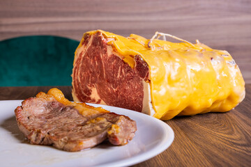 Fetta di carne frollata in cera d'api e cotta sulla brace fotografata con dietro il pezzo originale da dove è stata tagliata