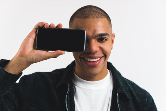 cheerful afro american boy holding a phone horizontally near his face, empty screen, medium closeup. High quality photo