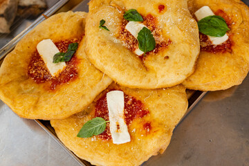 Montanare napoletane fritte e condite con sugo di pomodoro, mozzarella, basilico fresco e parmigiano esposte nel bancone da vendita di una pizzeria tradizionale napoletana 