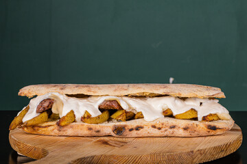 Panuozzo napoletano ripieno di salsiccia, patate al forno e mozzarella servito su un tagliere di legno in un pub napoletano