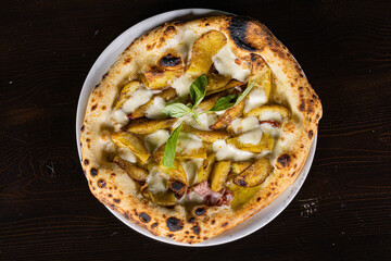 Pizza tradizionale napoletana con patate al forno, salsiccia, mozzarella e basilico fresco servita in una pizzeria