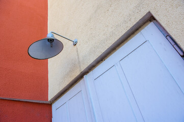 Hellblaue Aussenlampe aus Blech vor hellblauem Holztor und roter Wand