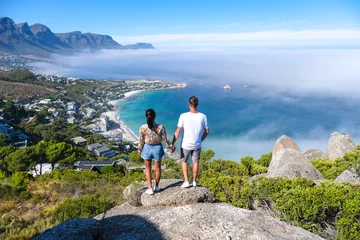 Foto auf Acrylglas Tafelberg a couple of men and women at The Rock viewpoint in Cape Town over Campsbay, view over Camps Bay with fog over the ocean. fog coming in from the ocean at Camps Bay Cape Town South Africa
