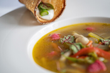 Selective focus of vegetables soup with asparagus, mushroom and pink (beetroot) gnocchi in a white plate. Bread variation on the edge on the plate. Vegetarian food. Gourmet restaurant.
