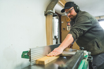 Medium shot of a carpenter using a table saw to cut a plank of wood while working in his woodworking studio. High quality photo