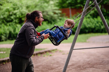Obraz premium Little toddler boy happily rides on swings and playing with tall long haired man in glasses