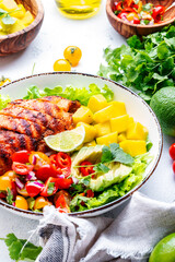 Yummy salad with grilled chicken fillet with mango, spicy salsa, tomatoes, cilantro, red onion and lettuce in tex-mex style, white table background, top view