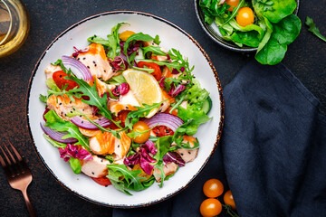 Gourmet salad with grilled salmon with tomatoes, cucumber, arugula, radicchio, red onion and lettuce with lemon oil dressing. Healthy lunch. Brown stone table background, top view