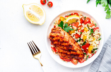 Grilled chicken fillet with bulgur tabbouleh salad with colorful tomatoes, parsley and lemon dressing, white table background, top view