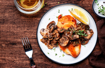 Fried chicken breast with mushrooms and onion sauce with white wine and thyme on plate, old wooden table background, top view