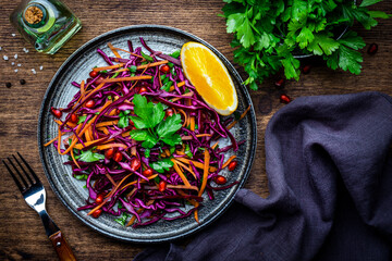 Coleslaw red cabbage salad with carrot, parsley, pomegranate and orange  with olive oil dressing on wooden kitchen table background, top view